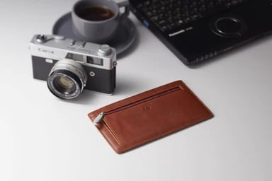 テーブルに置かれた、エイジの長財布（ブラウン）とフィルムカメラ、コーヒー、ノートパソコン