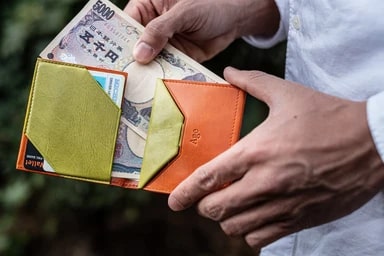 グリーンとオレンジのバイカラーの財布から五千円札を取り出す男性