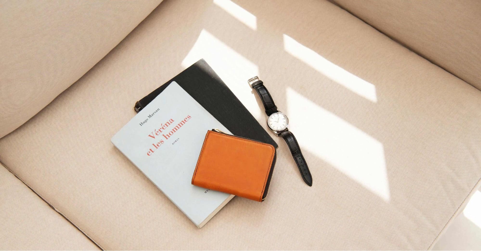 ソファーの上に本と腕時計とライトブラウンのＬ字ファスナー財布