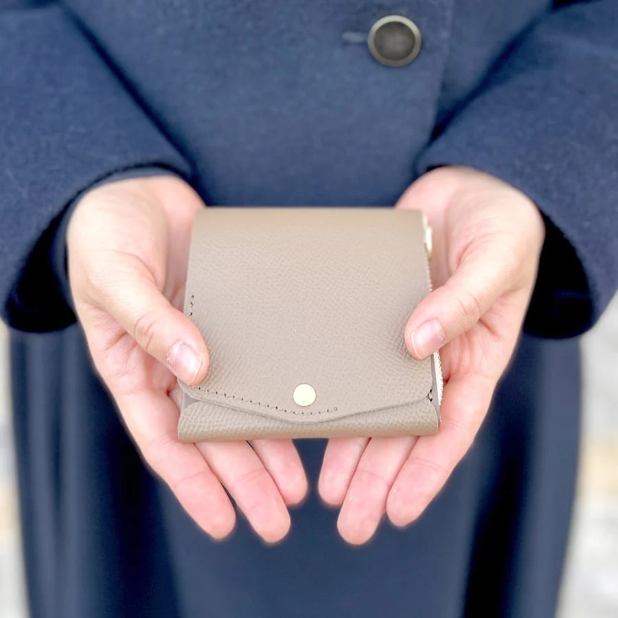 モクの小さく薄い財布（ベージュ）を両手で持つ女性