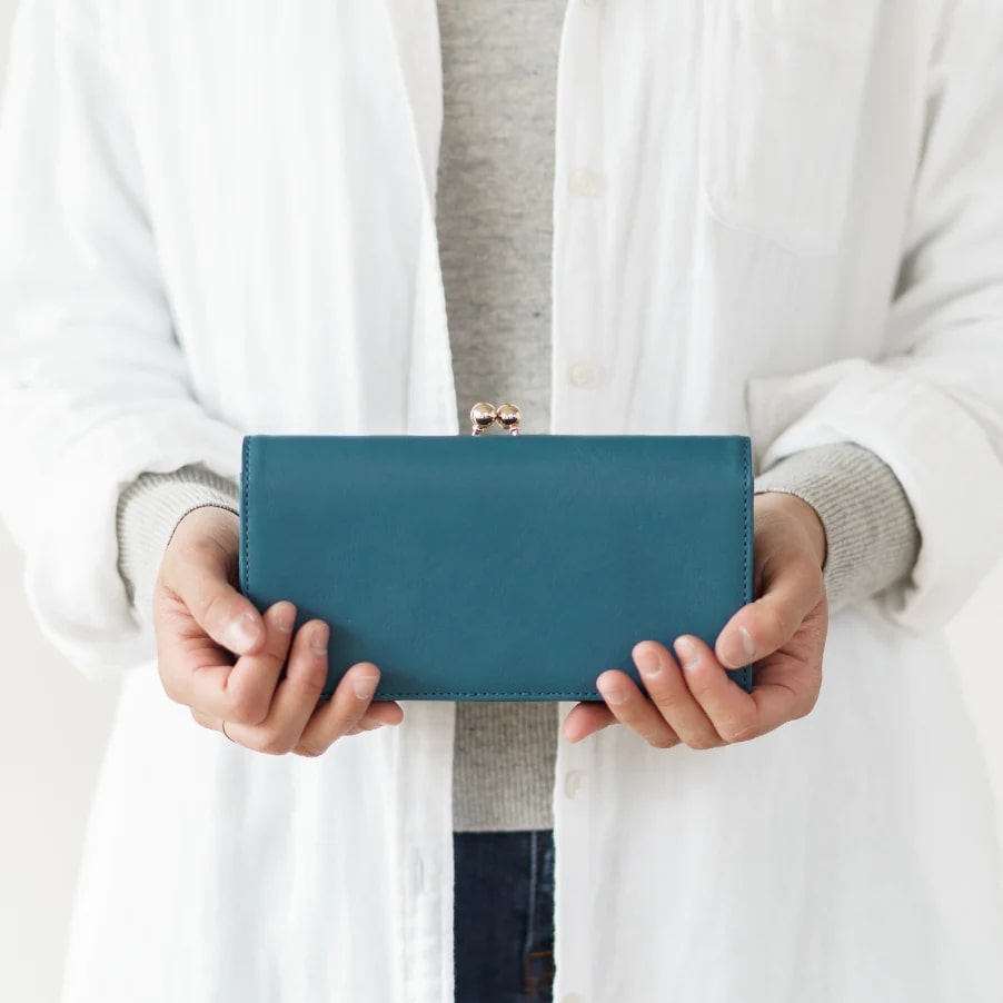 ムラ(mura）日本製高級シャンタン使用　牛本革がま口長財布（ブルー）を両手で持つ女性