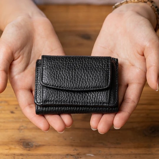ムラのイタリア製シュリンクイタリアンレザースキミング防止機能付き三つ折りミニ財布（ブラック）を手のひらに乗せる男性