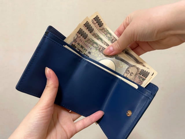 ネイビーの三つ折り財布に３万円を入れる女性の手
