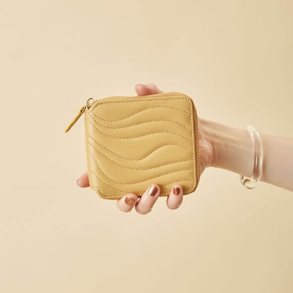 波状のステッチがポイントの二つ折り財布（サフラン）を持つ女性の手